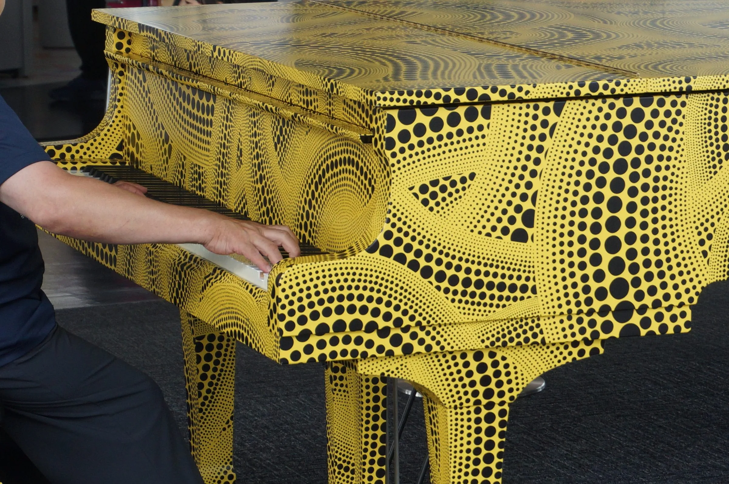 Hands playing a grand piano covered in a yellow and black polka-dot pattern