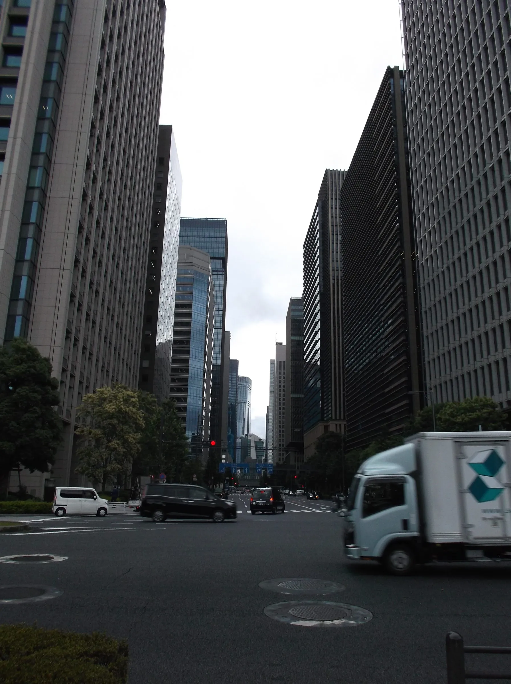 A broad avenue running between tall glass and stone office towers, with a delivery truck crossing the intersection on an overcast day