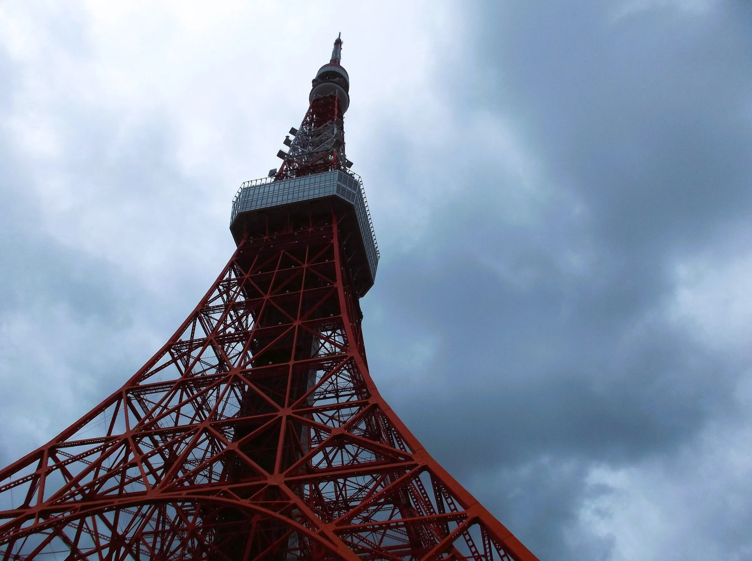 The red lattice legs and observation deck of Tokyo Tower seen from below against dark grey cloud
