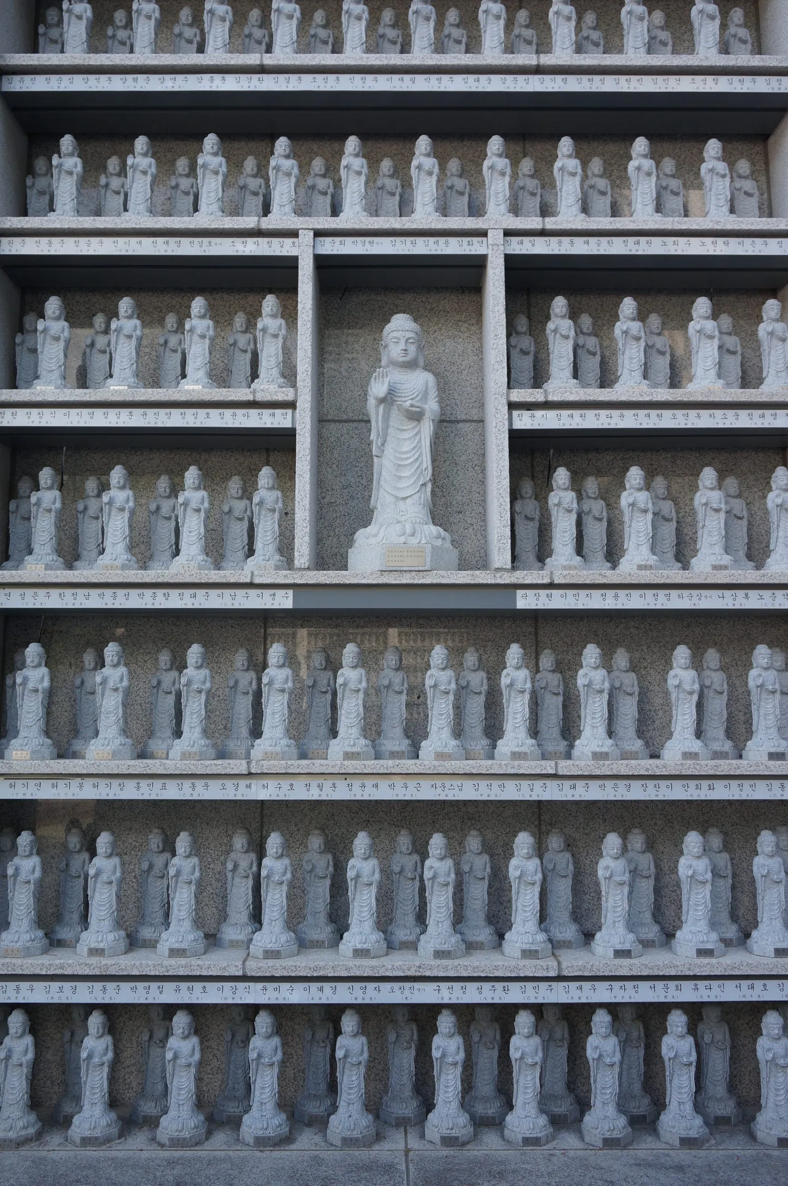 Shelves of small identical stone Buddha figures, each row lined with inscriptions, around a larger standing figure in the centre.